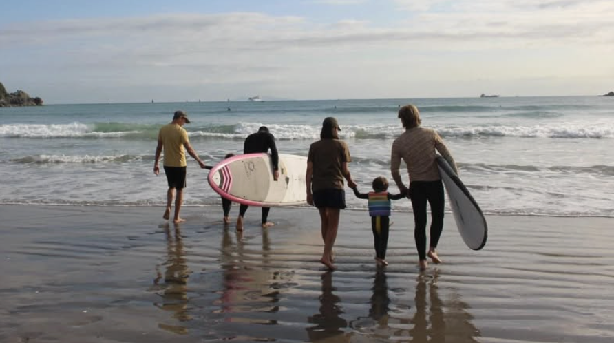 Volunteers and family walking back up the beach with surfboards